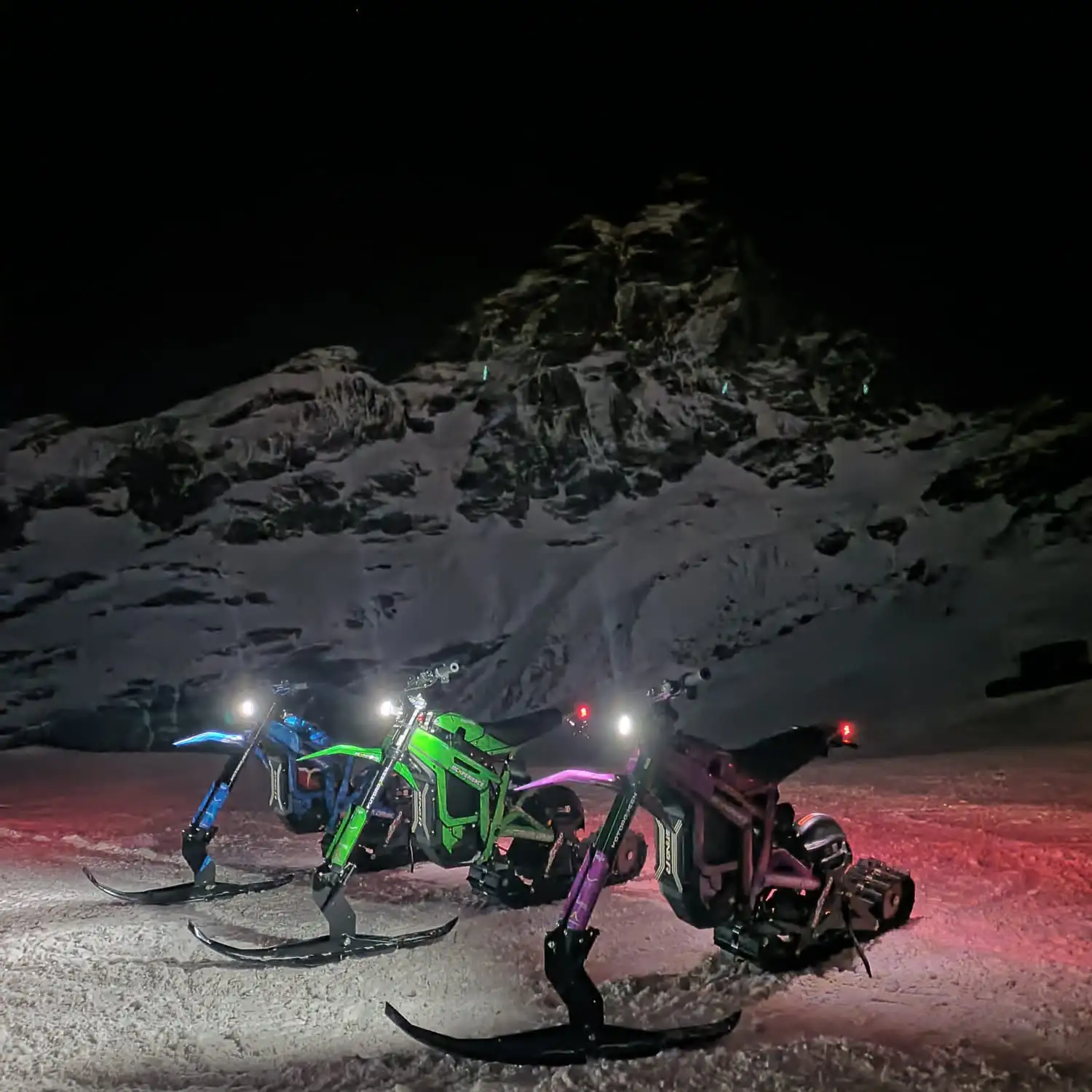 Snowbike illuminate davanti a un pendio innevato di notte